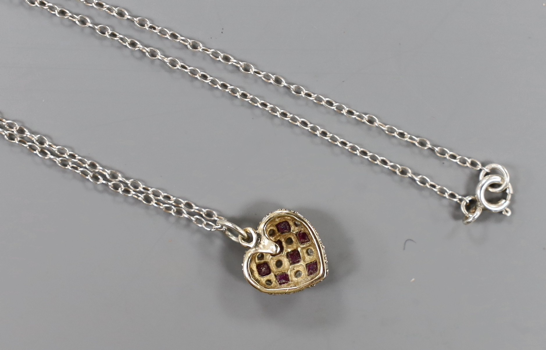 A modern yellow metal ruby and diamond set heart shaped pendant, 11mm,on a 925 chain.